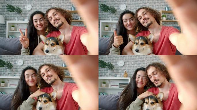 幸福的夫妇在家里与柯基犬自拍的肖像显示竖起大拇指