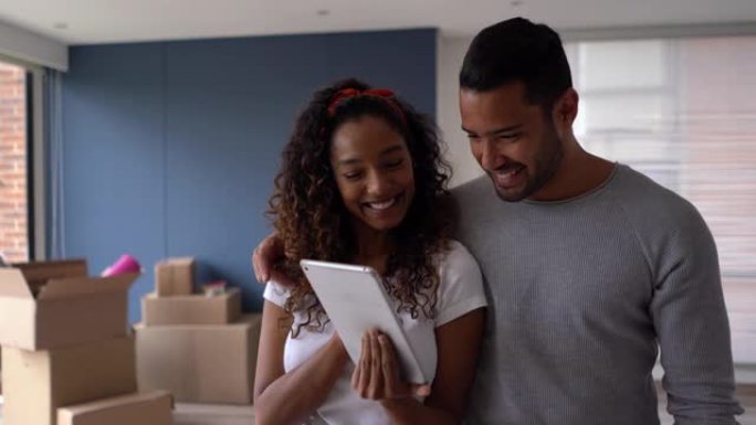 快乐的多元化夫妇搬进他们的新地方，看着平板电脑DIY创意，都微笑着