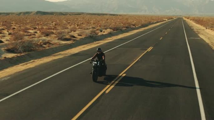 日落时在沙漠路上骑摩托车的人的鸟瞰图