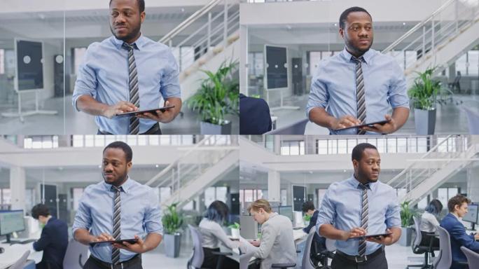 穿着衬衫走路的英俊年轻黑人经理用平板电脑通过他的业务同事，并监督他们的工作。在现代开放式办公室中，多