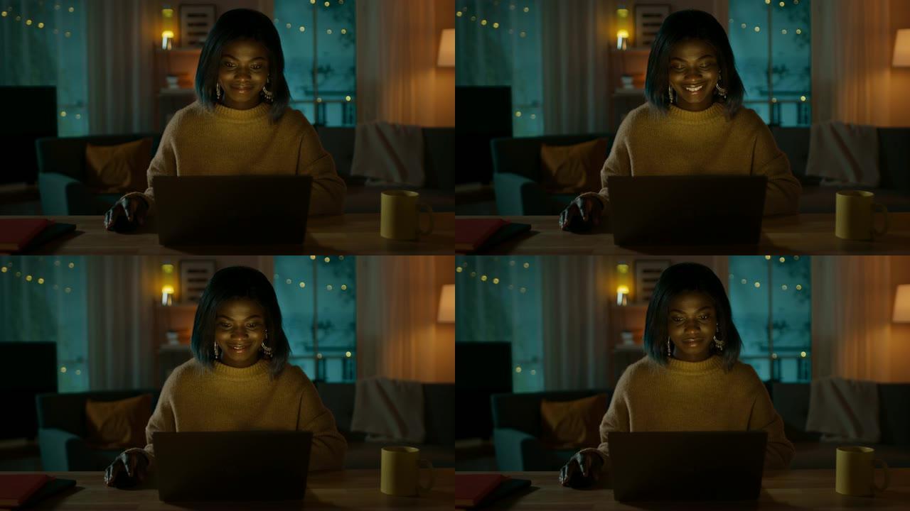 美丽微笑的非洲裔美国女孩坐在家里的办公桌前使用笔记本电脑的肖像。晚上，有创意的女人在舒适的客厅里用电