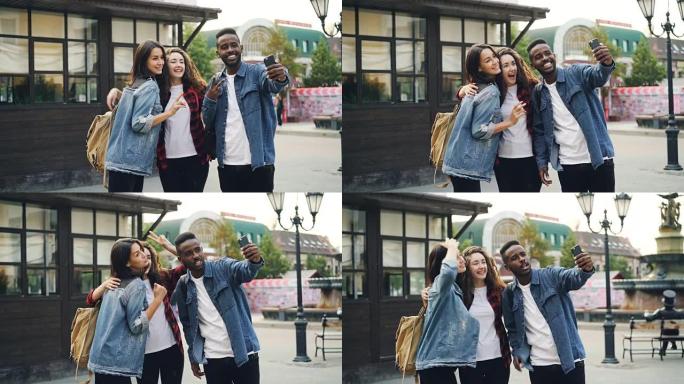 快乐的非洲裔美国人正在与朋友自拍，美丽的高加索女孩站在街上摆姿势，在国外旅行时拿着智能手机。