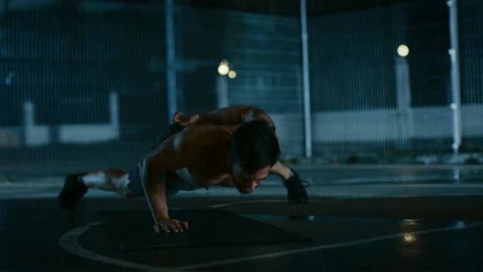 强壮的肌肉健康的光着膀子的年轻人正在做单手俯卧撑练习。他正在一个有围栏的室外篮球场里锻炼身体。居民区