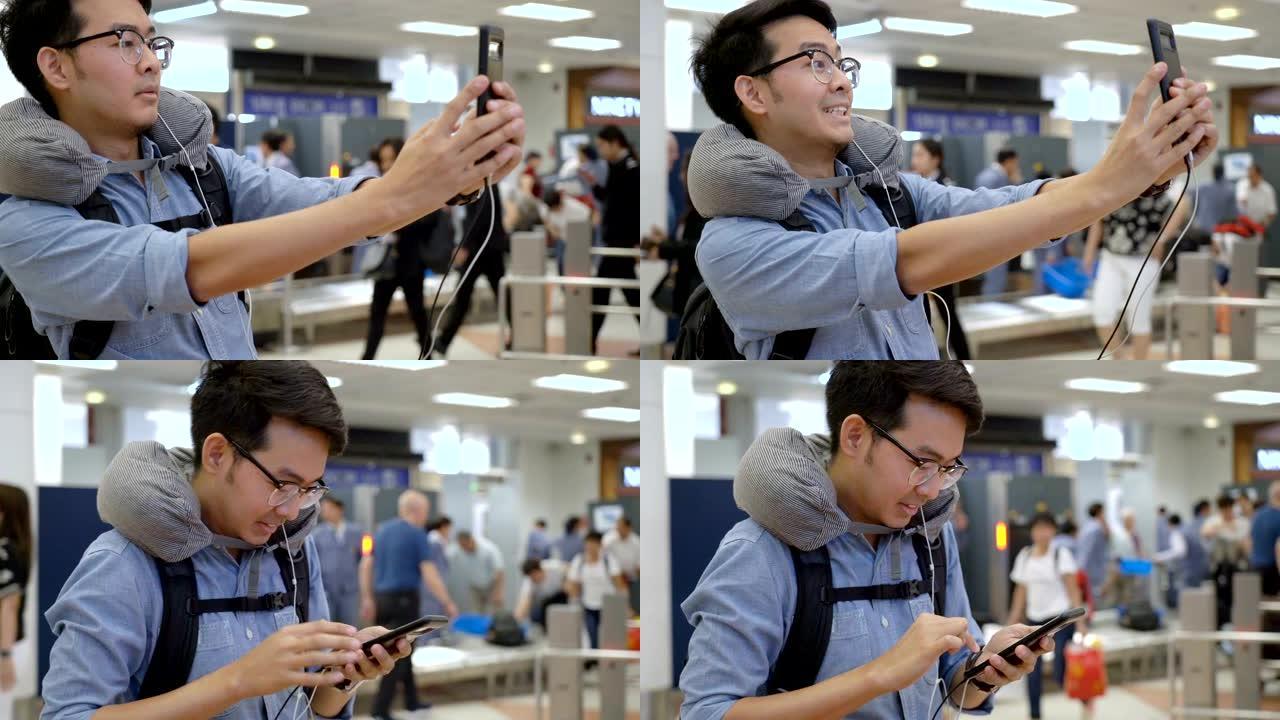 年轻的亚洲背包客博主男子在机场值机柜台自拍，配有旅行包和颈枕