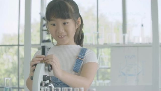 亚洲小女孩专心地看着桌子上的显微镜，小女孩做科学实验。有科教理念的人。