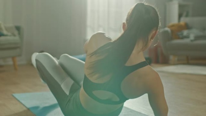 一位穿着运动上衣的美丽自信丰满健身女性的慢动作特写镜头正在她明亮宽敞的公寓里进行腹部锻炼，室内简约。