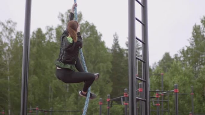 女运动员在公园的户外健身房攀岩绳