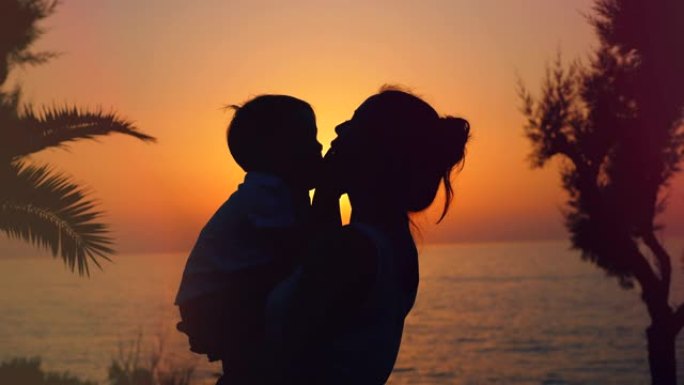 背光男孩和他的母亲在海上日落时拥抱