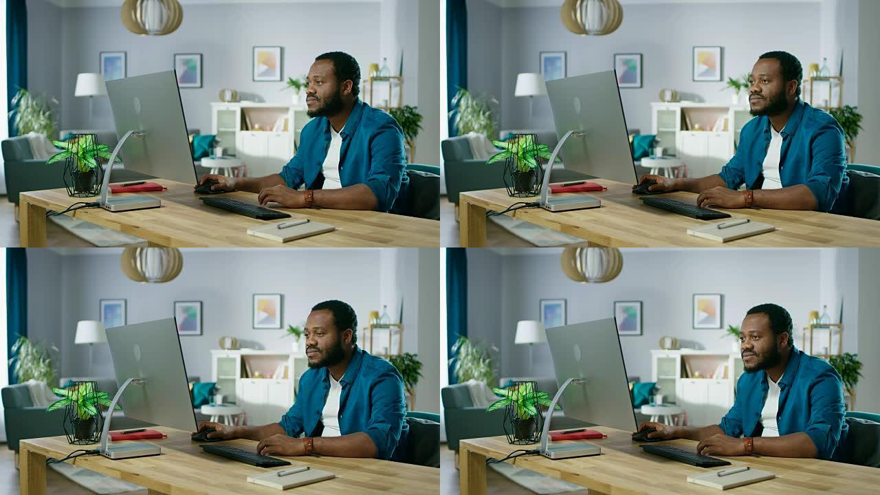 英俊的非洲美国人坐在他舒适的客厅的桌子旁，在个人电脑上工作。