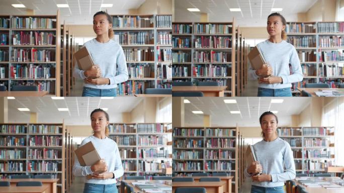 非裔美国女孩走在大学图书馆里，拿着书四处张望