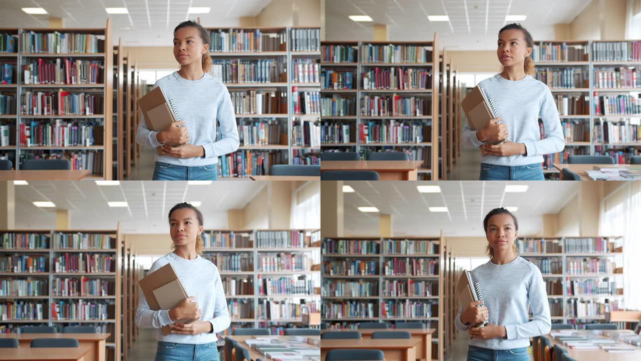 非裔美国女孩走在大学图书馆里，拿着书四处张望