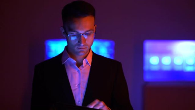 戴眼镜的男人在黑暗的房间里用平板电脑工作