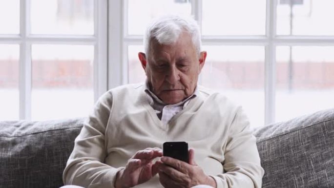 微笑的80年代祖父使用手机应用程序坐在沙发上