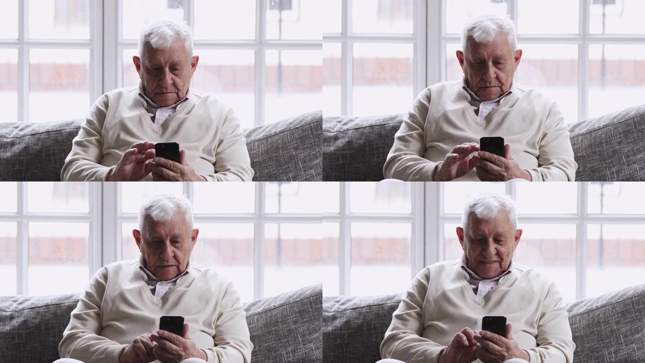 微笑的80年代祖父使用手机应用程序坐在沙发上