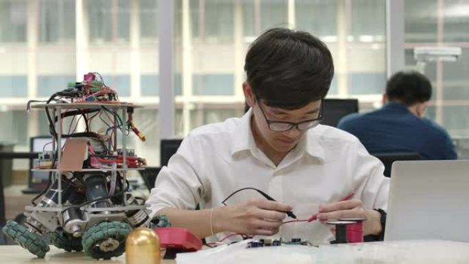 年轻的亚洲电子开发工程师与机器人一起工作，在车间的机器人原型电路中测量信号。有技术或创新概念的人。