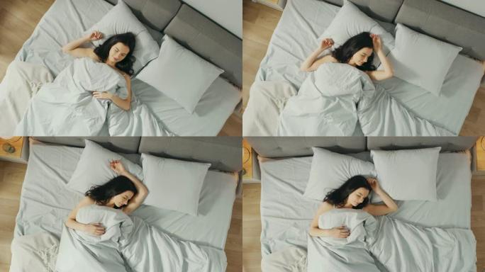 美丽的年轻黑发女人在清晨迷人地睡在她的床上。安静睡觉的女孩甜美温暖的景色。自上而下的相机拍摄。