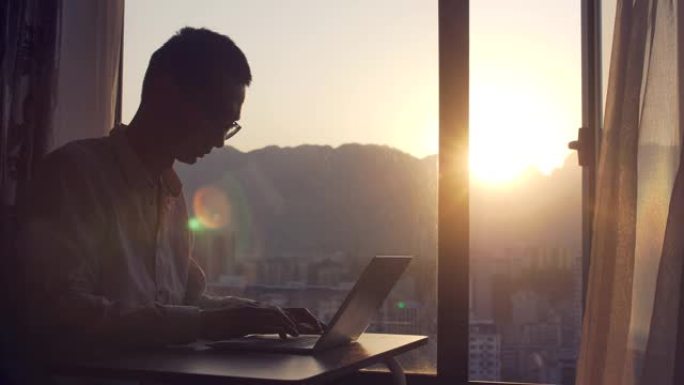 男子在日落窗前使用笔记本电脑