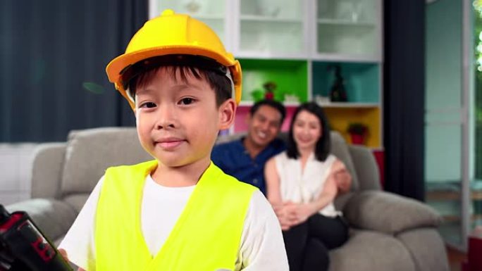 这位男孩戴着安全硬度和工作头盔的肖像，作为一名工程师站在父母面前玩耍。