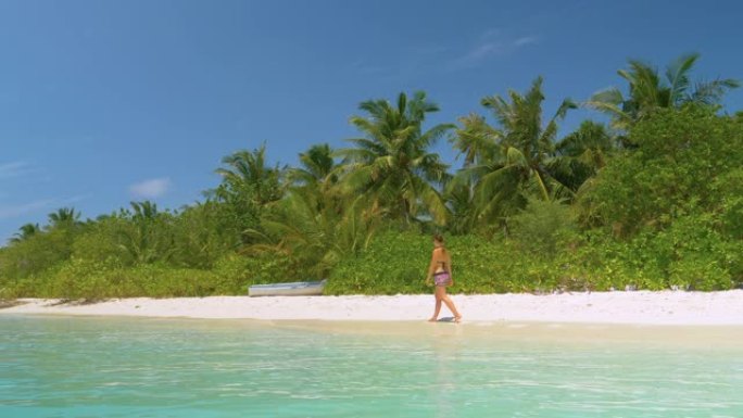 慢动作: 年轻女子在马尔代夫田园诗般的白色沙滩上漫步。
