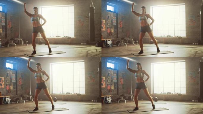 穿着运动上衣和短裤的强壮而健康的美丽运动女性正在阁楼风格的工业健身房进行站立运动，并配有励志海报。这