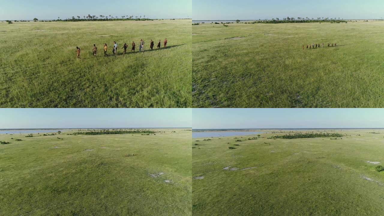 4k空中缩小了一群游客在博茨瓦纳Makgadikgadi草原上与San人/Bushman穿着传统服装