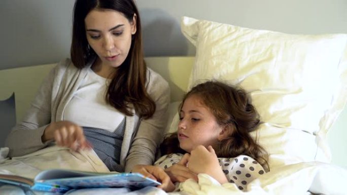 妈妈躺在床上为女儿读睡前故事。单身母亲定期给女儿读故事。带着爱，希望你的孩子快乐