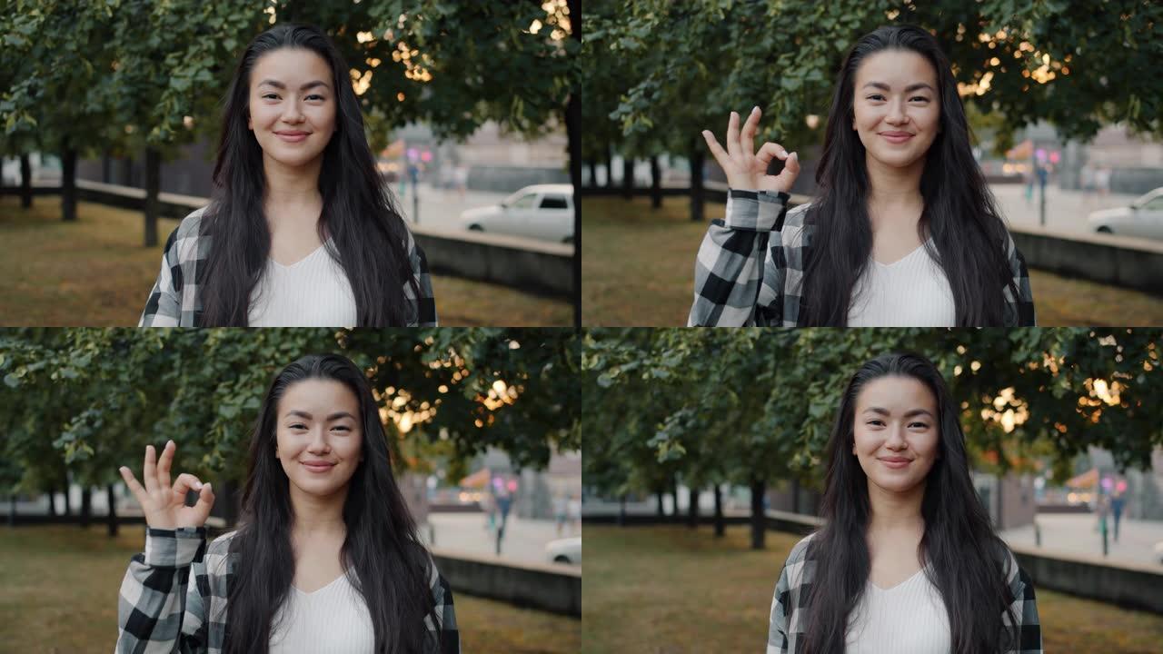 漂亮的亚洲学生在城市公园微笑着在户外展示OK手势