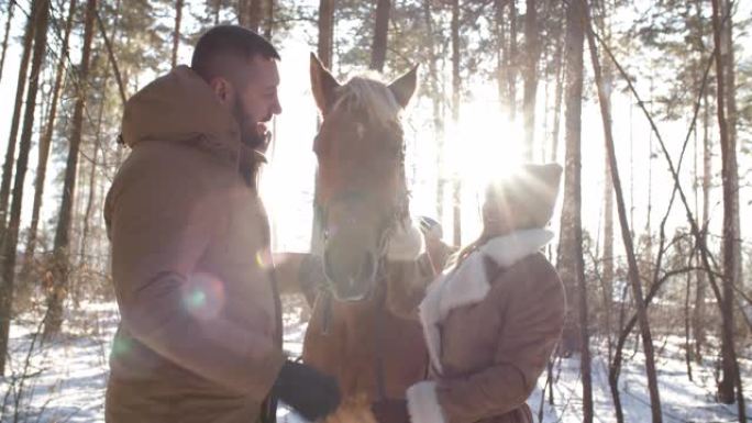 快乐的情侣爱抚马，冬日在森林里聊天