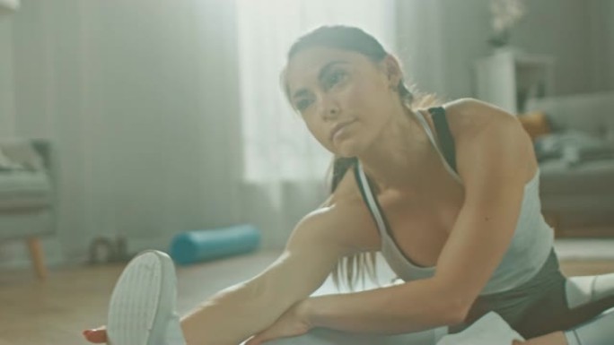 一个美丽自信的健身女孩在她明亮宽敞的客厅和舒适简约的室内做伸展瑜伽练习，穿着运动运动服。