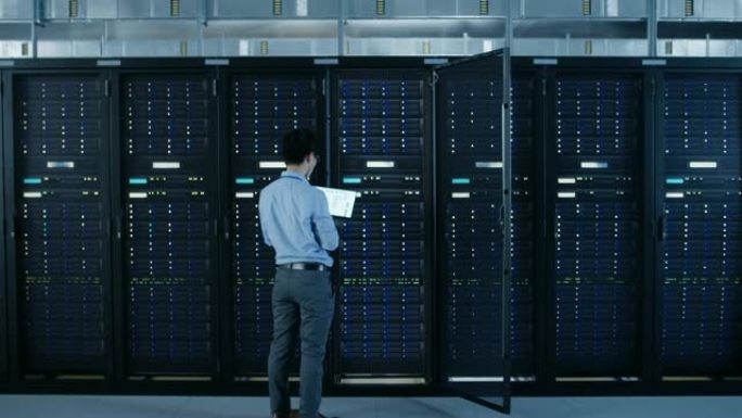 在现代数据中心: IT工程师站在开放式服务器机架机柜旁边，用笔记本电脑进行无线维护和诊断程序。缩小相