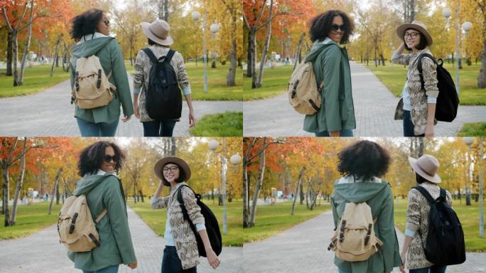 迷人女孩的慢动作朋友在城市公园背着背包散步。