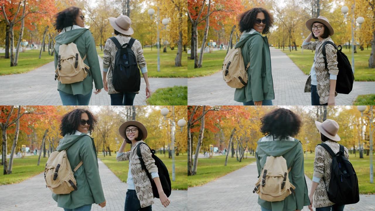 迷人女孩的慢动作朋友在城市公园背着背包散步。