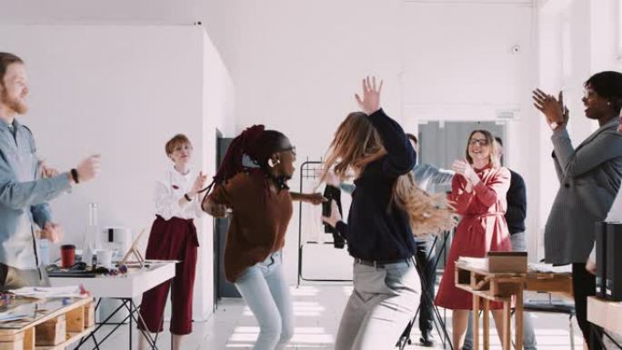 红色史诗-W 8К 两个快乐的多元化商业女性在办公室团队庆祝派对慢动作上做有趣的赢家舞蹈。