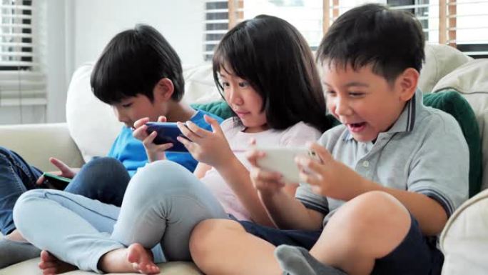 一群孩子连续坐在沙发上，在智能手机上玩电子游戏。一群孩子玩智能手机快乐有趣。早期教育d learni