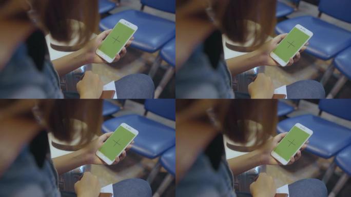 亚洲妇女在国际机场使用带有绿屏的白色手机设备。