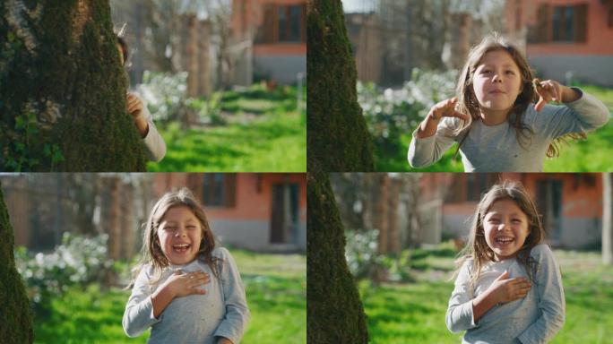 可爱的小女孩无忧无虑地躲在树后，在相机里笑得吓人的真实照片