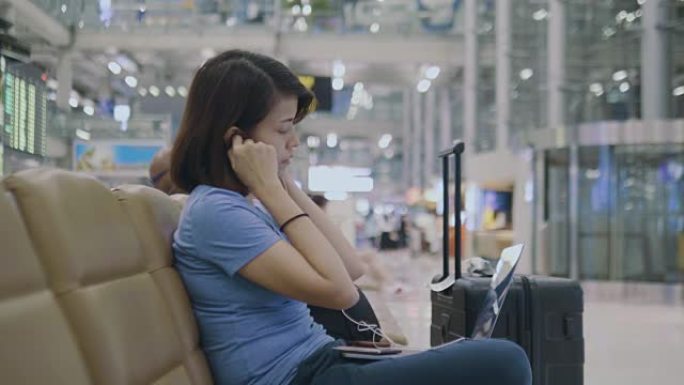 在机场候机室等候登机时，正在笔记本电脑上工作的旅游妇女。