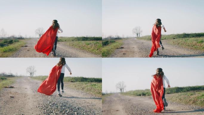 一个有趣的小女孩打扮成超级英雄的真实照片，穿着红色斗篷跑步，在阳光明媚的日子里玩得开心