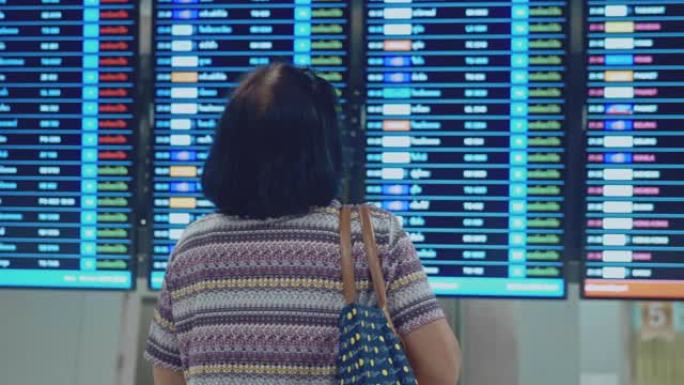 亚洲高级女性在抵达离境板上检查和查看航班