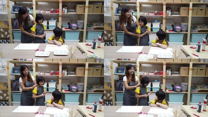 一位亚洲中国美术老师在美术课开始前为她的学生绑好围裙