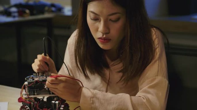 年轻的亚洲女性电子开发工程师与机器人一起工作，在车间的机器人原型电路中测量信号。有技术或创新概念的人