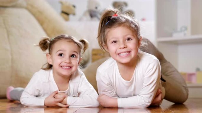 两姐妹躺在卧室地板上的肖像在背景中微笑着毛绒动物和玩具屋。