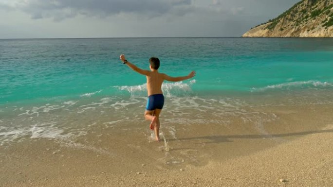 快乐的男孩在沙滩上玩绿松石水。在希腊凯法利尼亚享受假期