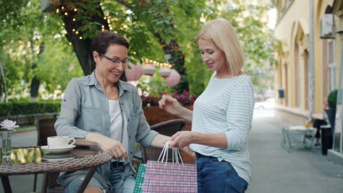 成熟的女人在街头咖啡馆遇见朋友，在购物袋中展示购物