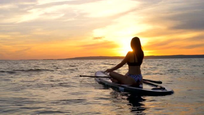 女孩在日落背景上冥想。女运动员在开阔的海洋中躺在冲浪板上。
