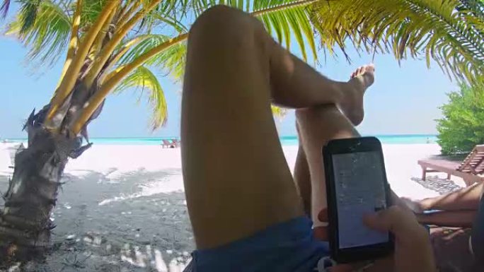 马尔代夫宁静海滩棕榈树下使用智能手机的CU个人视角