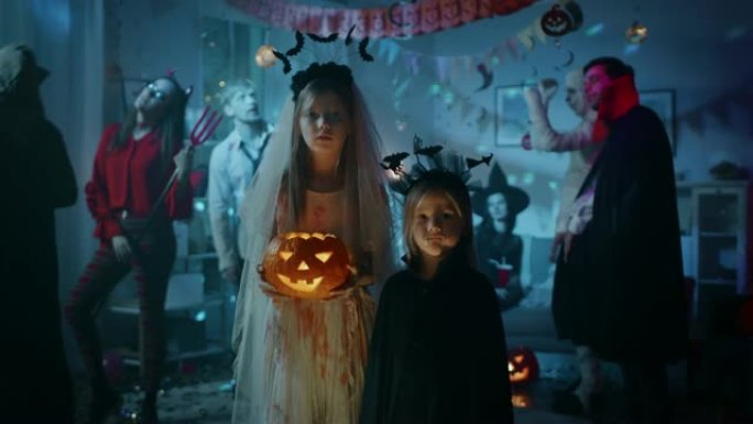 万圣节服装派对: 肖像女孩穿着血腥的白色新娘礼服，拿着可怕的娃娃站在可爱的小吸血鬼蝙蝠妹妹。在怪物跳