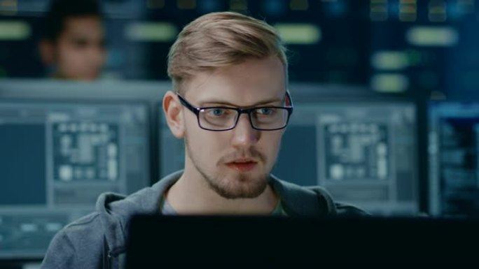 戴着眼镜的聪明英俊的IT专家的肖像可以在个人计算机上工作。在技术研究数据中心中带有屏幕的背景下未聚焦