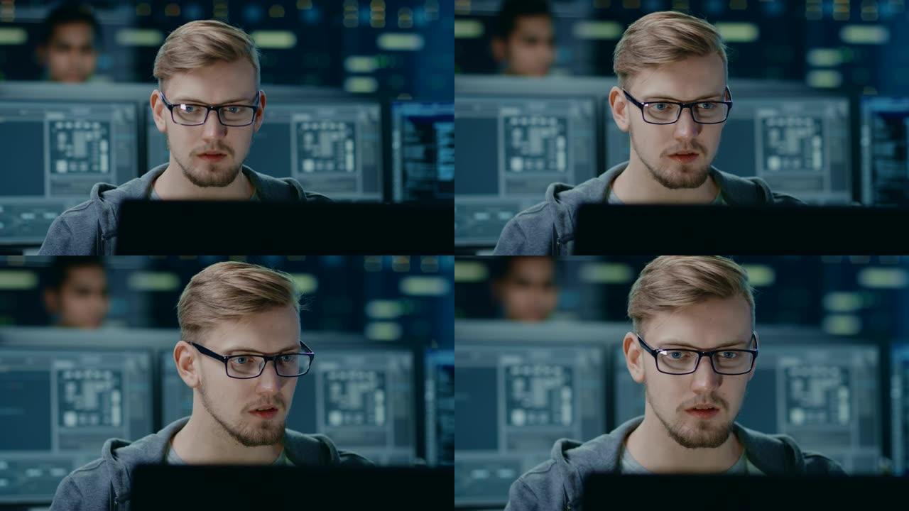 戴着眼镜的聪明英俊的IT专家的肖像可以在个人计算机上工作。在技术研究数据中心中带有屏幕的背景下未聚焦