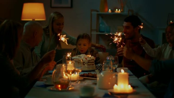 生日庆祝可爱的小女孩在餐桌上，母亲带来蛋糕，女孩吹灭蜡烛。在餐桌上，快乐的亲戚和朋友聚集在一起庆祝。